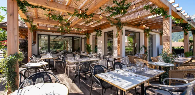 terrasse avec tables dressées sous pergolas en bois et végétaux