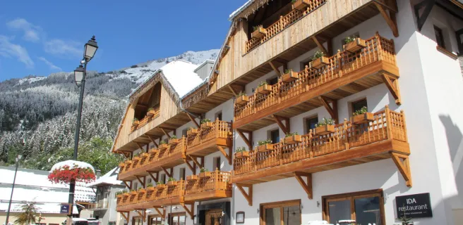 Bâtiment blanc avec balcons en bois, sol et sapins enneigés